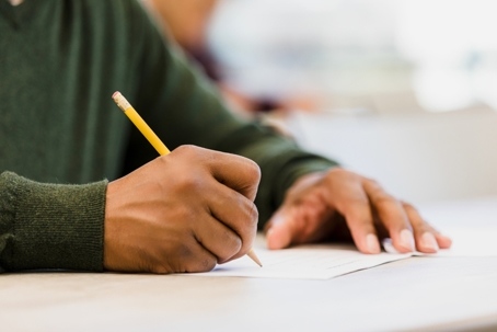 A close-up of a person writing on paper with a pencil. | Monument Immigration