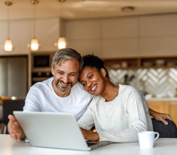 a couple looking at the screen of a laptop with a coffee mug on their side